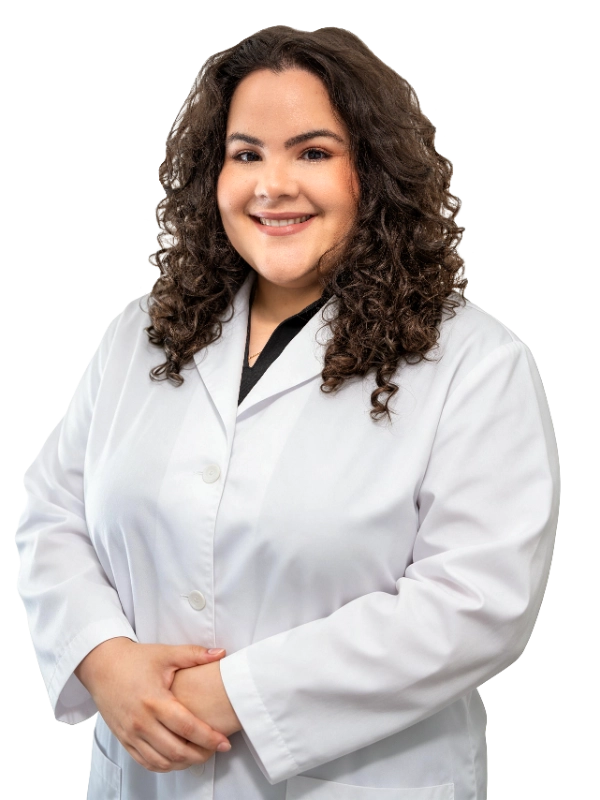 VTC_DrFernandez_Cutout_Coat_2562x3416_optimized Professional portrait of Dr. Hanen Fernandez, MD, a healthcare provider wearing a white lab coat over dark scrubs, photographed against a black background. Dr. Fernandez has long curly brown hair and presents a warm, approachable smile with hands clasped in front, exemplifying the professional demeanor expected of medical staff specializing in interventional procedures.